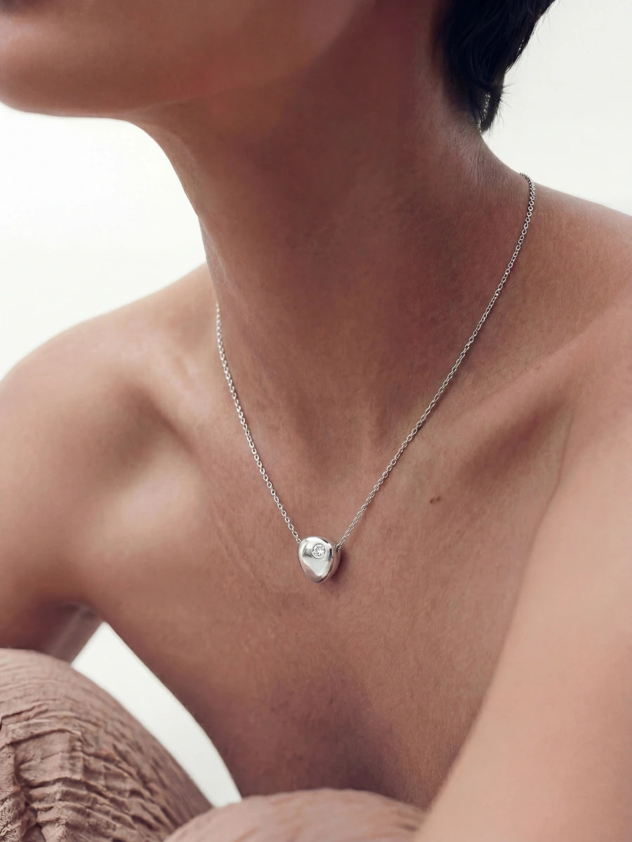 Necklace with a heart-shaped pendant worn by a person against a neutral background