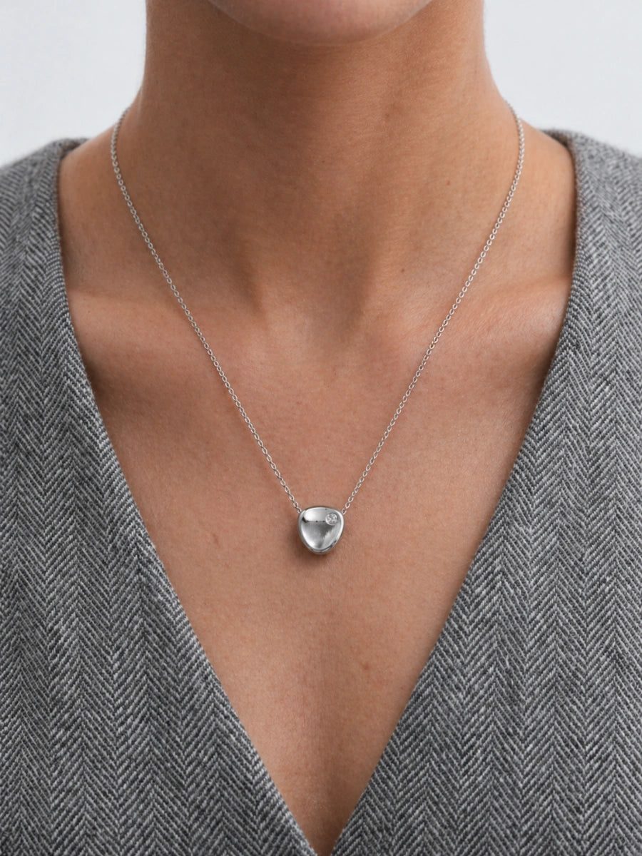 Silver heart-shaped pendant necklace on a person wearing a gray sweater.