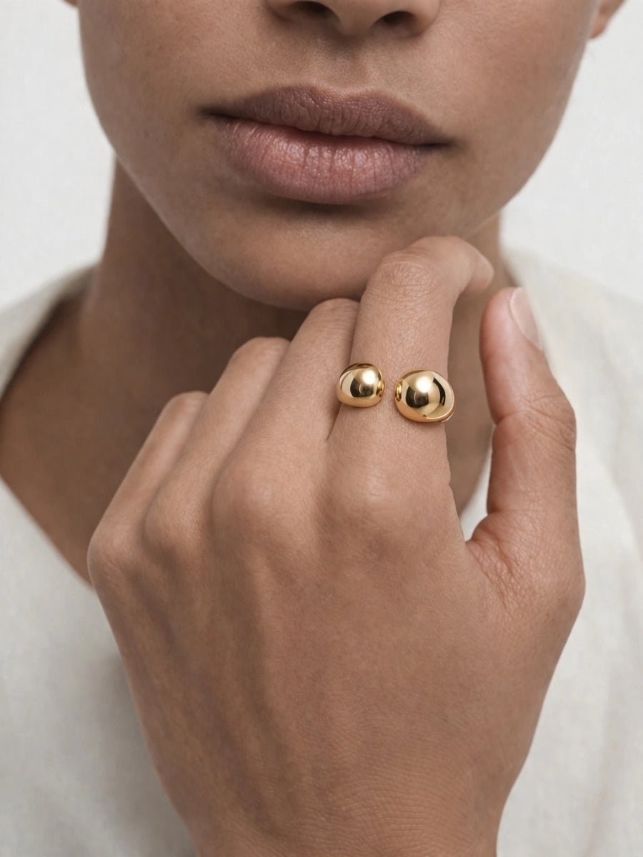 Close-up of a hand wearing two gold rings on a neutral background